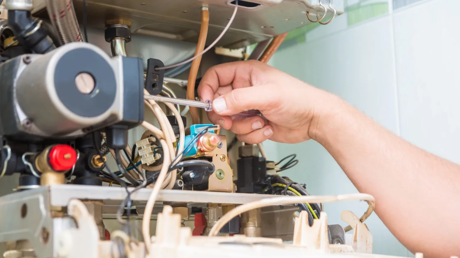 Technician troubleshooting the control compartment of a home heating unit with a screwdriver